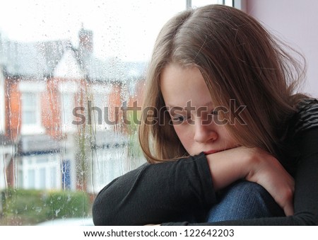 A young girl sad on her window close to tears
