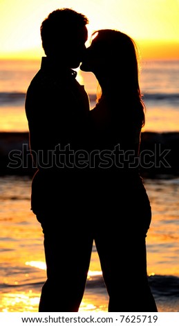 Silhouette of a young couple kissing at the beach with the sun setting behind them