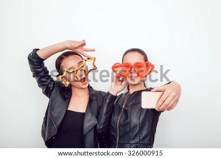 Asian girls in the funny sunglasses. They pose, grimace and look at the camera. Hair removed. The skin is clean. They make a picture on the phone. Leather jackets.