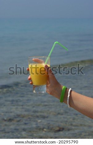 Glass of juice in human hand with sea on background