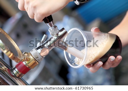 Pouring dark beer to plastic glass from beer tap