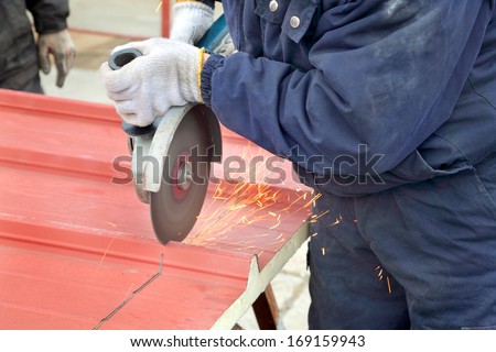 Cutting of heat insulated galvanized corrugated sandwich roof panel, workers hands angle grinder tool