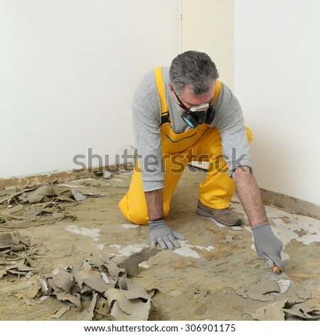 Adult worker with protective mask remove glue and rubber with putty knife from floor