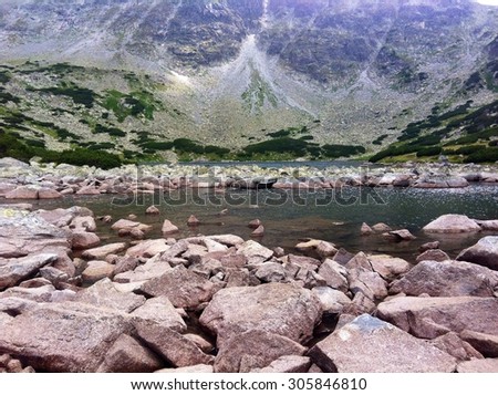 Landscape image of cold mountain lake in summer with stone rocky shore and horizon beneath a peak
