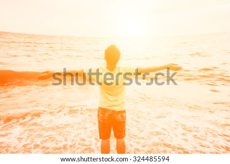 happy man standing one the beach with arms outstretched at sunri
