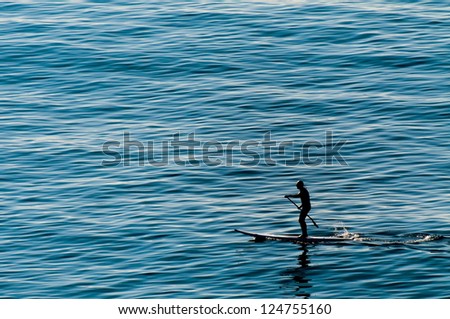 A man rowing standing on a surf table on the deep blue sea