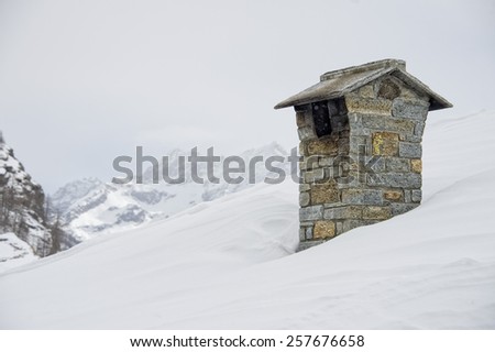 mountain house roof with smoking chimney on the deep white snow background