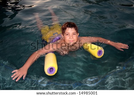 A young boy floats quietly in a pool with the aid of pool noodles. Brown eyes.