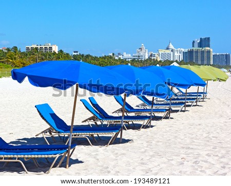 Colorful umbrellas and lounge chairs on Miami Beach with visible city skyline. Famous vacation destination.