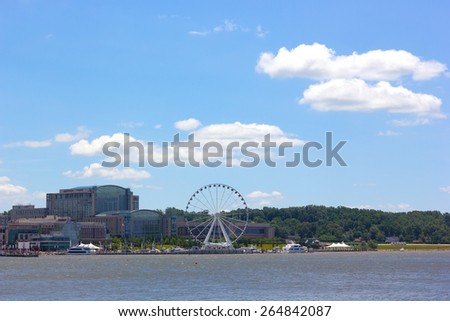 National Harbor photographed from Woodrow Wilson Memorial Bridge. National Harbor waterfront with Ferris wheel under a blue cloudy sky in Maryland, USA