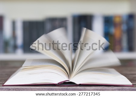 Opened book in front of bookcase with flying pages and motion blur with selective focus.