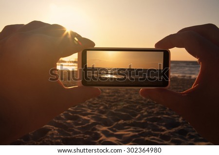 Man taking a photo of a sunset at sea with his phone - point of view shot