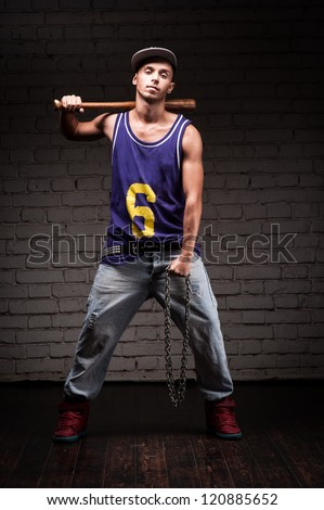 hip-hop style man holding baseball bat and chain over dark brick wall on background