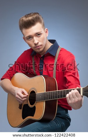 caucasian young vintage man in red shirt playing guitar over blue background