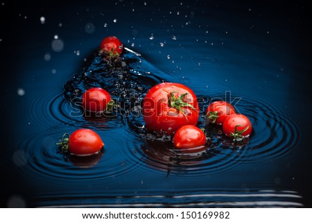 small group of fresh tomatoes falling in water over blue background