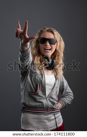 young cheerful casual caucasian woman with headphones in black sunglasses over gray background