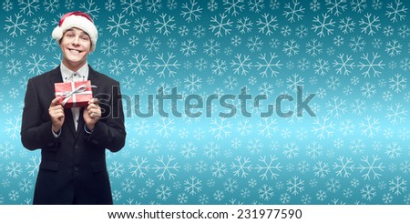 smiling young business man in santa hat holding christmas gift over winter snowflakes background