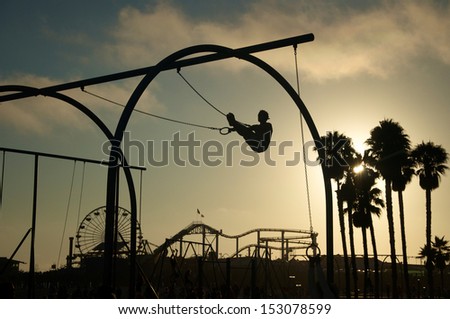 As the sun sets a silhouetted man works out on gymnast rings