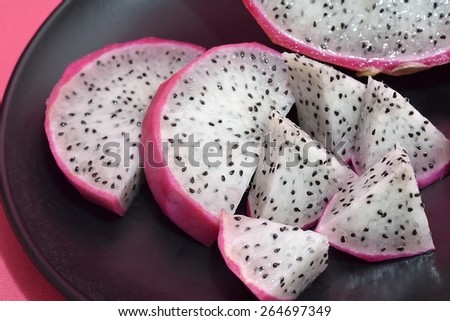dragon fruit cut into pieces, in a black plate on a pink background, closeup