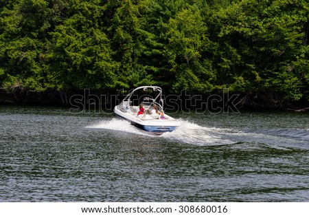 PORT CARLING - AUGUST 19: Young mother with two children driving a pleasure boat along the shoreline on Indian River in Port Carling, Ontario on August 19, 2015