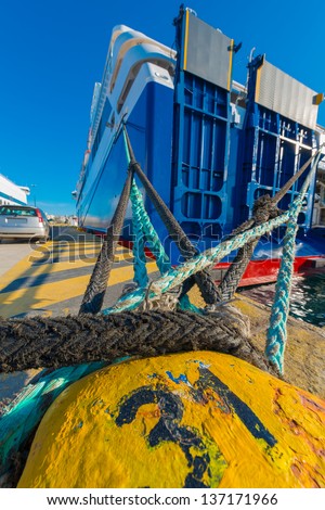 Greece Piraeus,Yellow rusty metal bollard and ship rope harbor at sunny day with ships in background