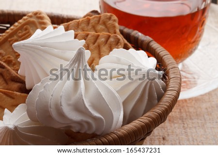 marshmallows and cookies in a basket next to a cup of tea