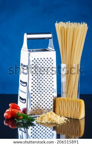 cheese, grater, spaghetti, tomatoes on a black reflective surface