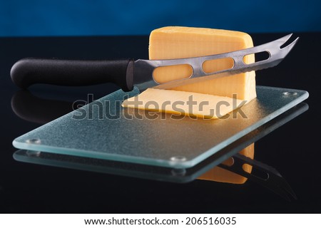 a piece of cheese on a glass cutting board with a knife