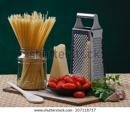 cheese, grater, spaghetti, tomatoes, parsley and garlic on a kitchen table