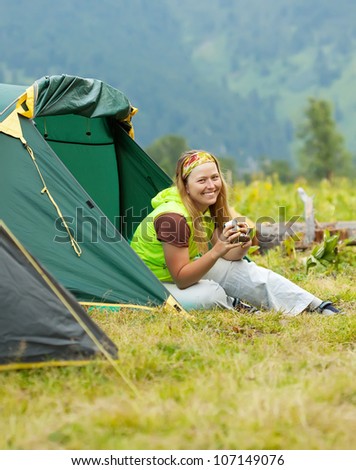 Happy female hiker drinking tea in front camp tent