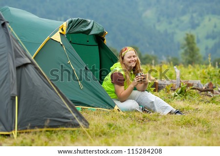 Happy female tourist drinking tea in front camp tent