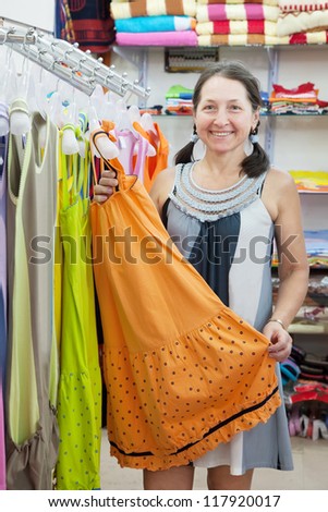Mature woman  chooses dress at fashionable shop