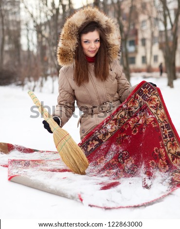 woman cleans red carpet with snow in winter outdoor