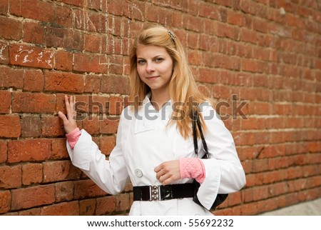 Pretty girl in white cloak near red brick wall