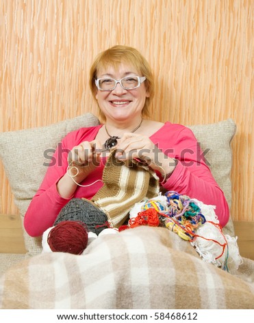 senior woman knitting with knitting-needle on sofa at home