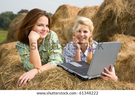 country girls resting with laptop on fresh hay bale