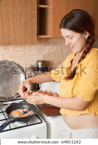 Young woman adds eggs to hot skillet. One of the stages of preparation of bacon and eggs.  See series