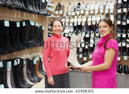 Two women chooses high boots at shoes shop