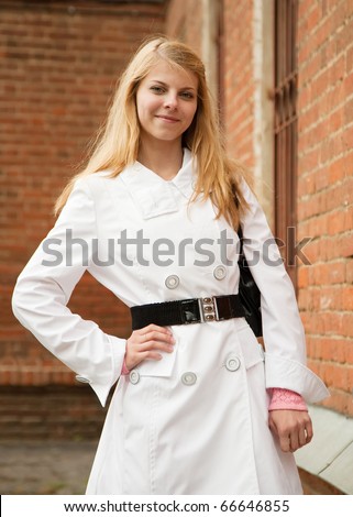 Pretty girl in white cloak near red brick house