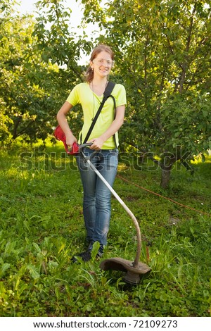 young woman is fixing lawn trimmer  in garden
