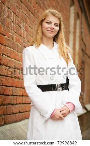 Pretty girl in white cloak near red brick wall