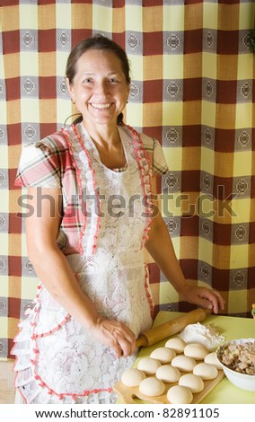 elderly woman cooking meat pasty with rolling pin at kitchen