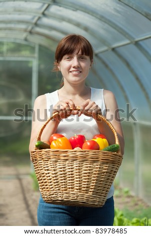 Young woman with basket of harvested vegetables in greenhouse