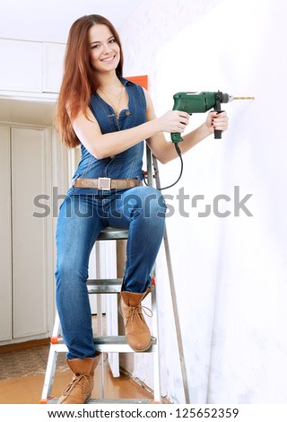 woman in overalls with drill makes repairs in home