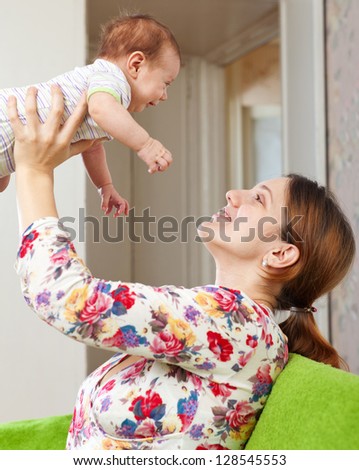 Happy mother holds to her baby over home interior background