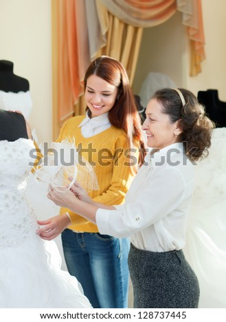 saleswoman helps bride chooses bridal gown at shop of wedding fashion. Focus on mature
