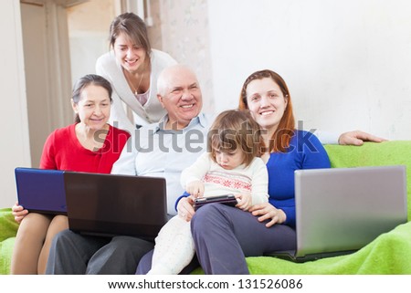 Happy multigeneration family uses few various portable devices in home interior