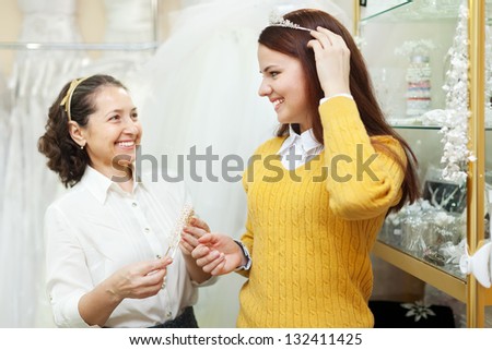 Mature saleswoman helps bride chooses bridal accessories at shop of wedding fashion. Focus on girl