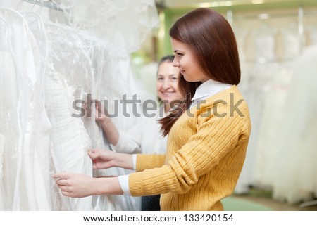 mother  with daughter chooses white gown at shop of wedding fashion