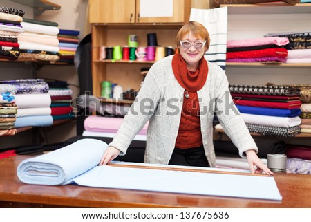 Mature salesclerk measures the fabric in a fabric shop